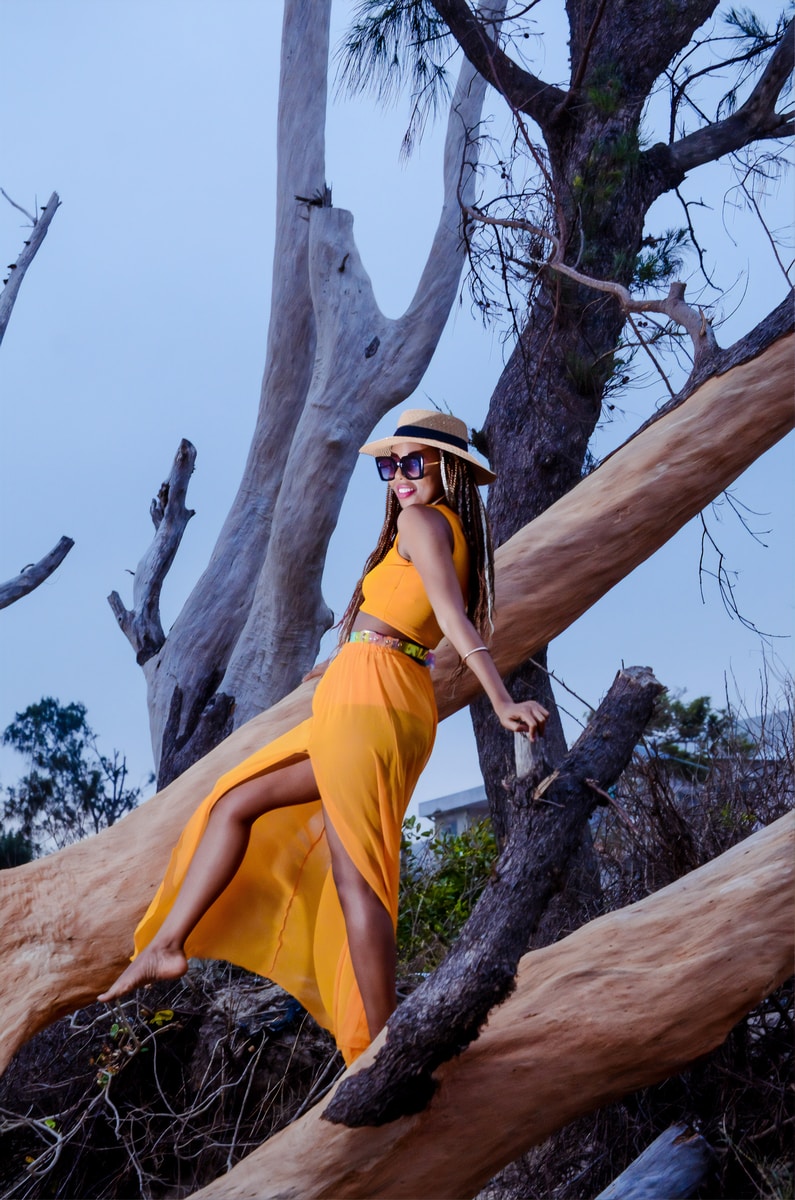 woman in yellow dress climbing on brown tree during daytime