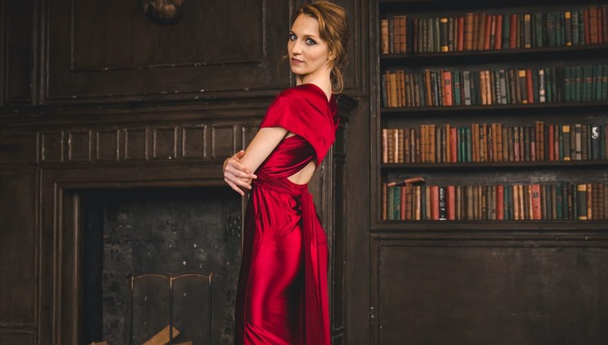 woman in red long sleeve dress standing beside brown wooden book shelf