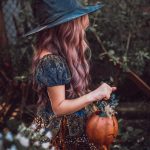 woman in black hat and brown dress holding pumpkin