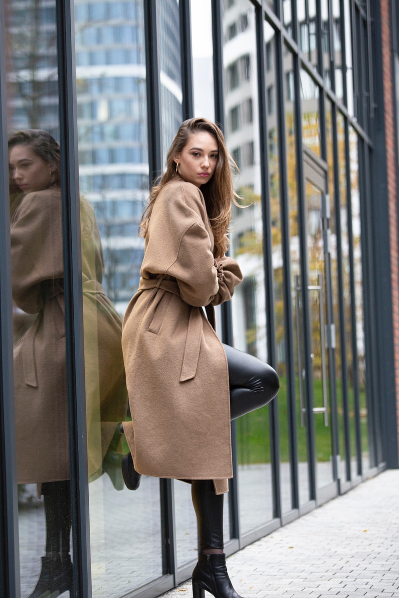 woman in brown coat standing near glass window