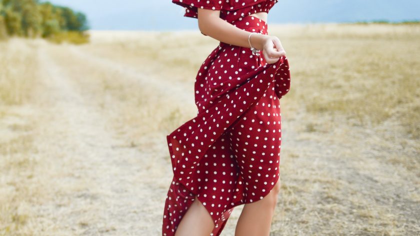 woman in red polka-dot dress standing in the middle of grass field during daytime