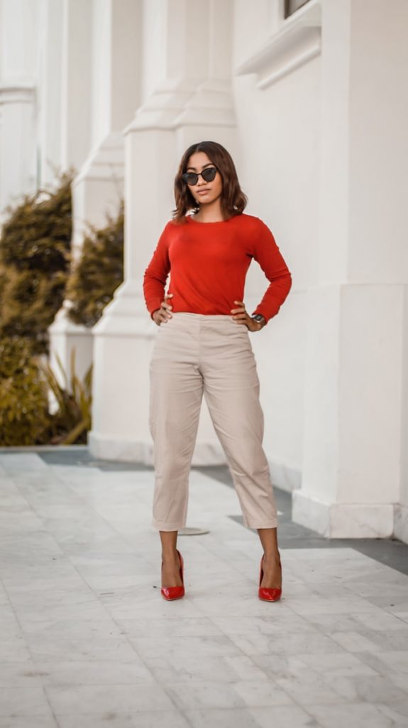 woman in red long sleeve shirt and brown pants standing beside white wall during daytime