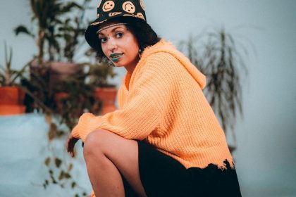 woman in orange knit sweater and black skirt sitting on ground