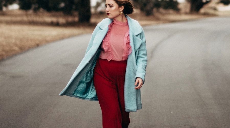 woman wearing teal coat and red pants walking on gray top road at day time