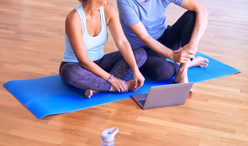 man in white tank top and gray pants sitting on blue yoga mat