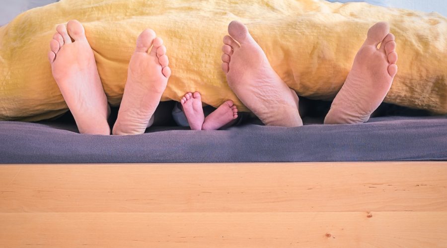 three people underneath yellow bed blanket