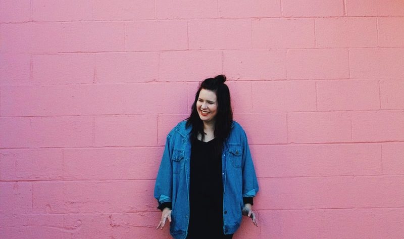woman standing beside pink brick painted wall