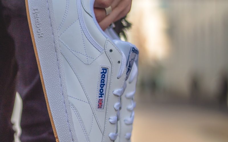 person carrying white Reebok low-top sneakers