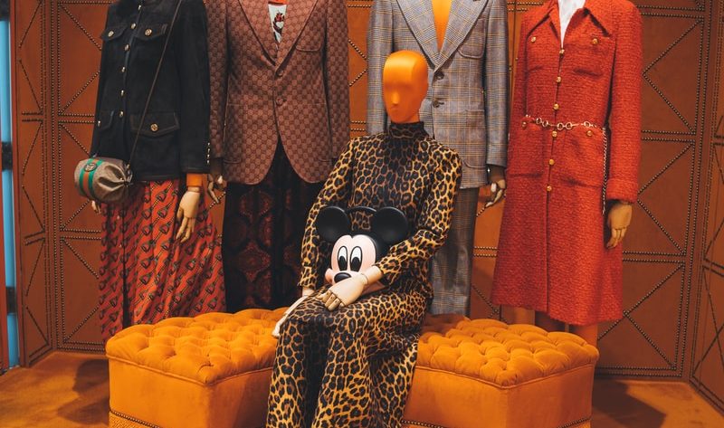 four mannequins wearing formal suits and another female mannequin wearing brown leopard long-sleeved dress sitting on tufted orange ottoman